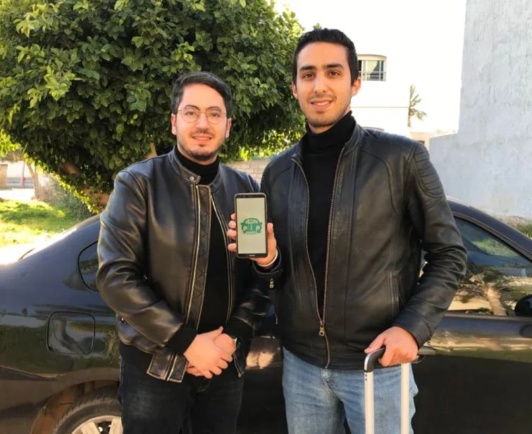 Les deux cofondateurs de Pip Pip Yalah devant une voiture, l’un présentant l’application sur son smartphone